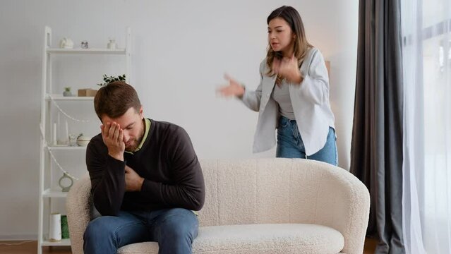 Aggressive woman screaming at scared husband at home. A man holds on his chest, feeling heart pain