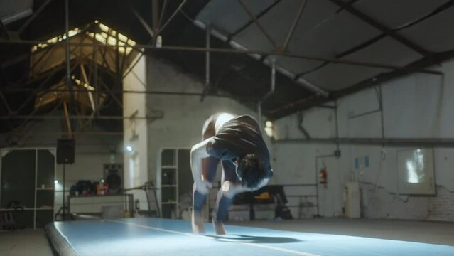 Young male gymnast practicing stunts on exercise mat in a gym, mastering skills for sports competition or performance