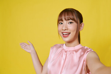 Dreamy cute young lady recording self video showing arm empty space isolated on yellow background