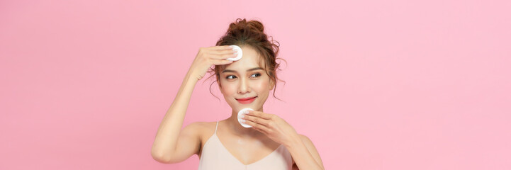 Smiling pretty young woman cleaning her face, using cotton pads and cleansing product - 703077080
