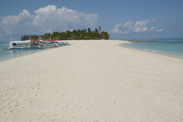 Beautiful white sand beach with palm trees on a hot, clear day and local traditional Filipino boats or Outrigger boats anchored.