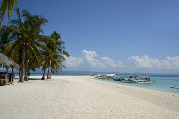 Obraz premium Beautiful white sand beach with palm trees on a sunny, hot, and clear day.