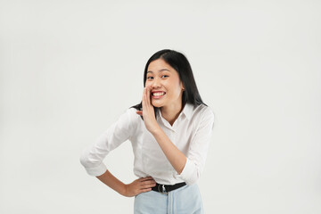 An Asian woman in a white blouse leans forward with her hand cupped to her mouth, as if whispering or sharing a secret. She looks playful against a white background.