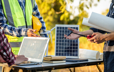 engineers discussing a solar energy project with a small solar panel model on the table, a laptop,...