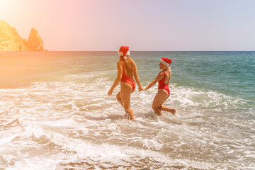 Women in Santa Claus hats run into the sea dressed in red swimsuits. Celebrating the New Year in a...