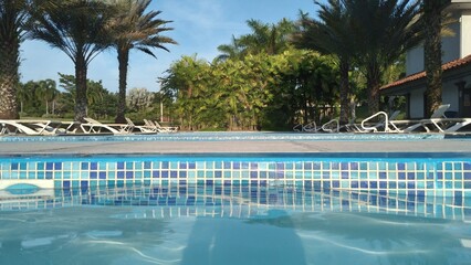 swimming pool with palm trees on a summer day, reflection of the sun in the water, point of view from inside the pool