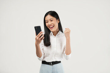 Portrait of a young Asian woman holding her phone feeling excited and celebrating, wearing a white t-shirt and isolated on a white background. 