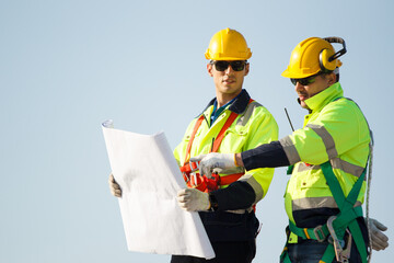 Senior professional engineers in full protection suit discuss on a blueprint paper on factory or building rooftop. Technicians inspecting the installation on rooftop. © DG PhotoStock