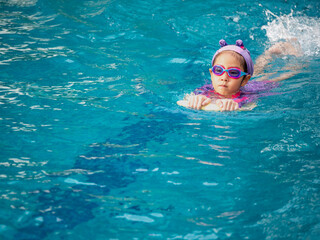 Asian child or kid girl wearing swimming suit to learning on swimming pool , learn and training swim on kick board