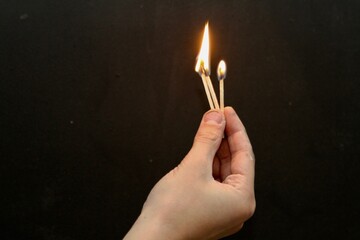  Hand holding three lit matches against dark background