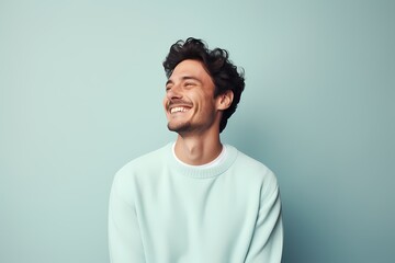 A man beaming happily in a pastel blue sweater on a pale mint-green background.