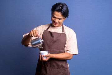 Smiling barista with brown apron serving and pour coffee from coffee pot into a cup. 