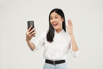 Photo of a young Asian woman wearing a white shirt, taking a selfie on a smartphone, video chatting...