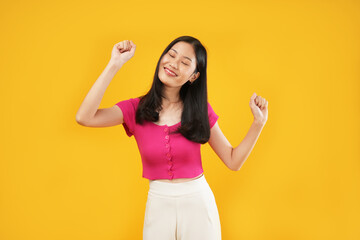 Portrait of a young Asian woman sign yes finally I gained it! A young woman wearing a pink t-shirt and showing white teeth, models isolated on a yellow background. 