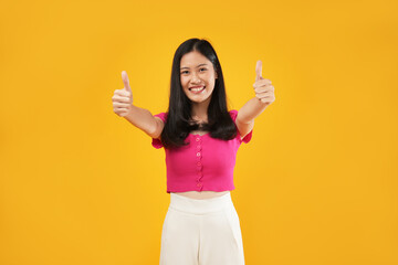 Photo of a young Asian woman smiling and raising her thumb with expressive facial expressions. Isolated on a yellow background. 