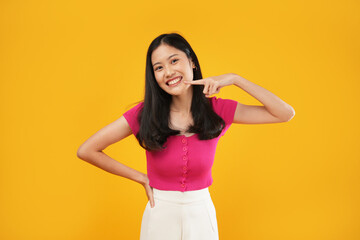 An Asian woman poses confidently with one hand on her hip and the other pointing to her face,...