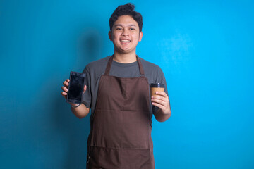 Asian barista man in brown apron hold craft cup coffee to go with blank screen mobile phone
