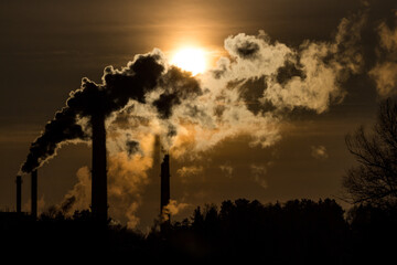 Silhouette of heavily smoking tall chimneys against the backdrop of the bright sun