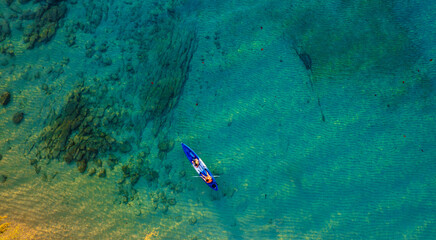 Top view of a woman paddling a yellow and orange kayak on the surface water blue sea. Woman doing...