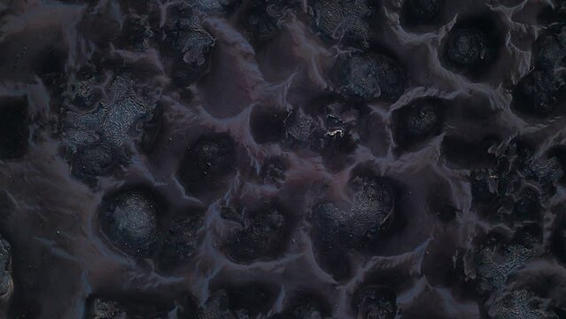 Zenithal rotate satellite view of black and grey mounds of polluted toxic waste on dry landscape
