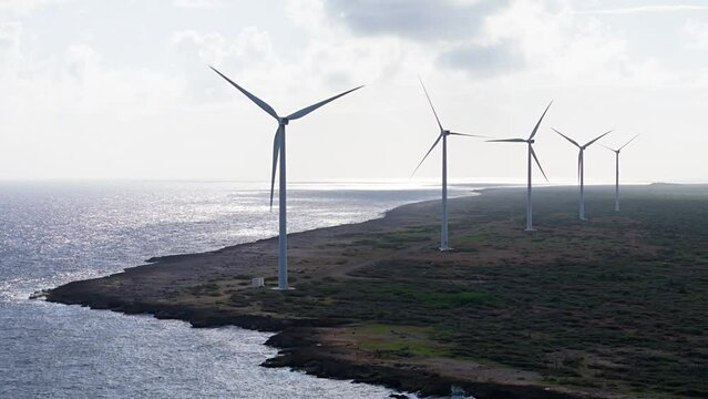 Row of wind turbines spin on north volcanic rocky coast of tropical island
