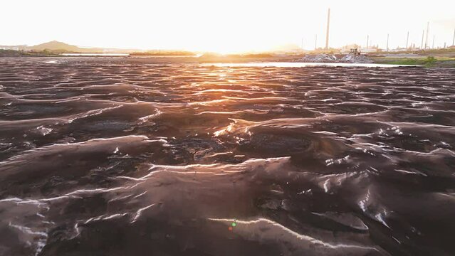 Aerial dolly above warped mounds in asphalt lake at golden hour sunset, environmental damage