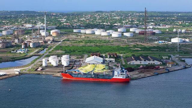 Large pile of sulfur offloaded from transport boat at dock with oil refinery flare stacks behind