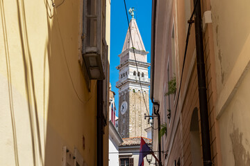 Stroll along narrow urban street that meanders its way towards magnificent St. George Parish Church. Old town of charming coastal town of Piran, Slovenian Istria, Slovenia, Europe. Sightseeing - obrazy, fototapety, plakaty
