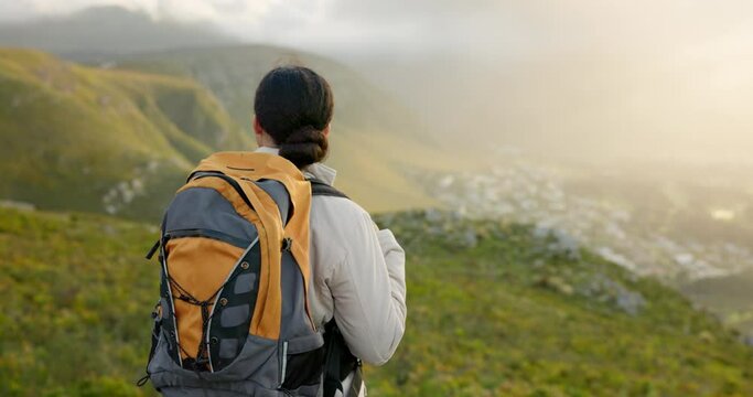 Back of woman, hiking and mountains for outdoor wellness, fitness and health in nature and cityscape. Sports person in wind with backpack and trekking on a hill for adventure, travel and eco journey