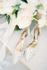 Bride shiny white pointed shoes stand on the marble step near the wedding bouquet