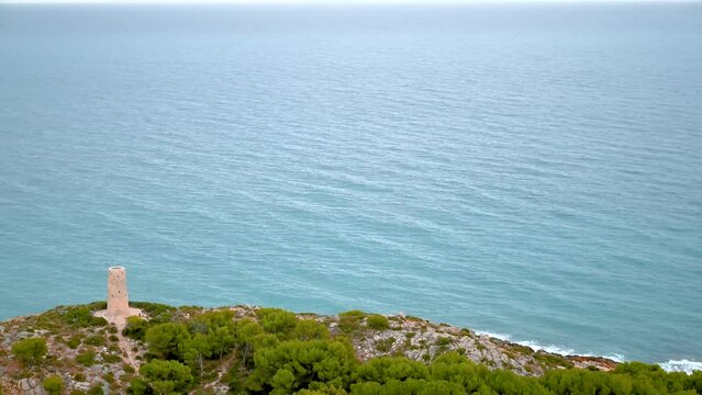 Horizontal 4K time-lapse of the Mediterranean Sea waves calmly arriving at the coastline by a defensive medieval stone tower in Oropesa del Mar, Spain