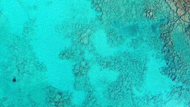 Drone view in Greece top view ocean clear blue water with rocks on the bottom a small white boat on a sunny day