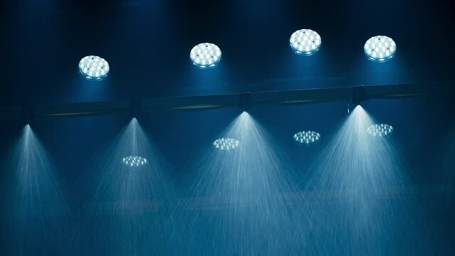 A special effects rain machine in a film cinema studio with a ceiling full of film lights. Sprinkler heads clearly visible with led music video lights are lighting the spray from behind.