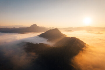 Aerial view of forest and mountain in fog with golden sunbeams at sunrise