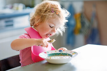 Adorable baby girl eating from spoon vegetable noodle soup. Healthy food, child, feeding and...