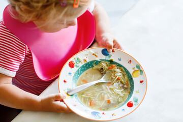 Adorable baby girl eating from spoon vegetable noodle soup. Healthy food, child, feeding and...