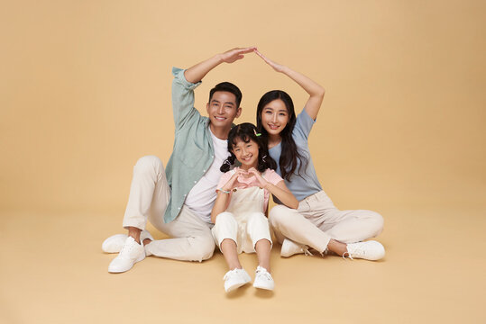 Happy asian family forming house roof with their hands at home. Insurance concept. happy family mother father and kids with roof isolated on nude color background.
