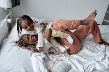 young caring mother adores her toddler, young woman and her kid cuddle on bed at home, full length...