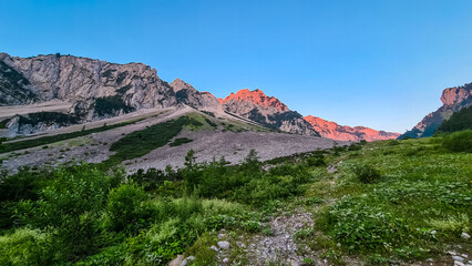 Scenic view of ridge Begunjscica at sunrise in untamed Karawanks, border Austria Slovenia, Europe. Hiking on Loibl Pass, Slovenian Alps. Steep mountains blazed crimson with first rays of morning sun