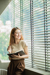 Photo of an attractive young Asian woman writing a diary. A freelance woman is relaxing in writing...