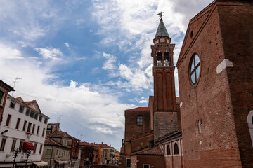 Fototapeta na wymiar Close up view of bell tower of Church of Saint James Apostle nestled in charming town of Chioggia, Venetian Lagoon, Veneto, Italy. Sightseeing in historic old town of Chioggia. Walking along canals