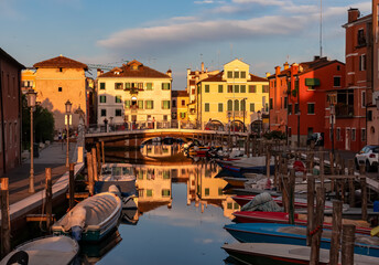 Fototapeta na wymiar Scenic view of peaceful canal Vena at sunrise in charming town of Chioggia, Venetian Lagoon, Veneto, Italy. Small boats floating in calm water. Enchanting reflections create atmosphere of tranquility