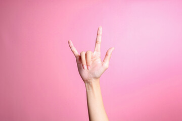 Hand showing rock sign with fingers gesture against pink background, human hand gesture - obrazy, fototapety, plakaty
