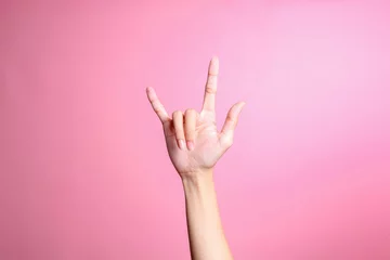Fotobehang Hand showing rock sign with fingers gesture against pink background, human hand gesture © Queenmoonlite Studio