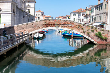 Breathtaking beauty of historical bridge Ponte Foscarini in town of Chioggia in the picturesque Venetian Lagoon, Italy. Calm atmosphere as the stunning water reflections grace the charming canal Vena