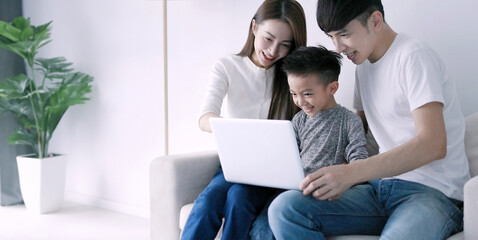Parents with child watching funny videos using laptop browsing online tv streaming enjoying spending time together  at home in living room sitting on sofa