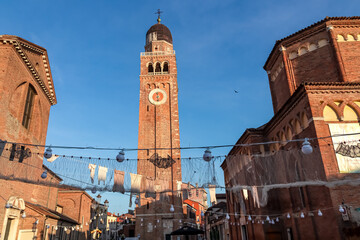 Sunrise view of bell tower of Cathedral Santa Maria Assunta in charming town of Chioggia, Venetian Lagoon, Veneto, Italy. Decoration Sagra del Pesce in foreground. First sun beams on landmark