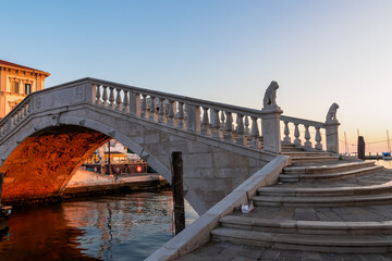 First rays of sunrise illuminate steps of bridge Ponte di Vigo stretching across the enchanting...