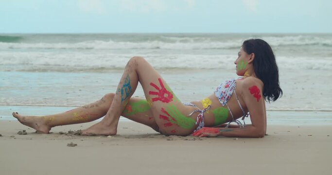 Vibrant body paint adorned the bikini-clad figure of a young girl, creating a striking scene on a Tropical beach in the Caribbean with ocean waves in the background