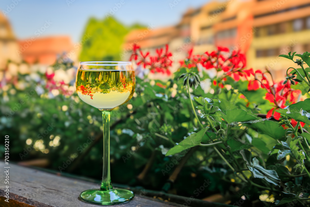 Wall mural a glass of gewurztraminer wine at an outdoor restaurant, blurred half timbered houses and flowers in